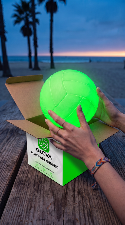 Lifting a glowing GLOVA volleyball out of its box on the beach at dusk